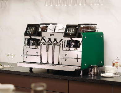 Una máquina de café profesional de Franke con dos pantallas táctiles y un panel lateral verde, sobre la barra de un bar