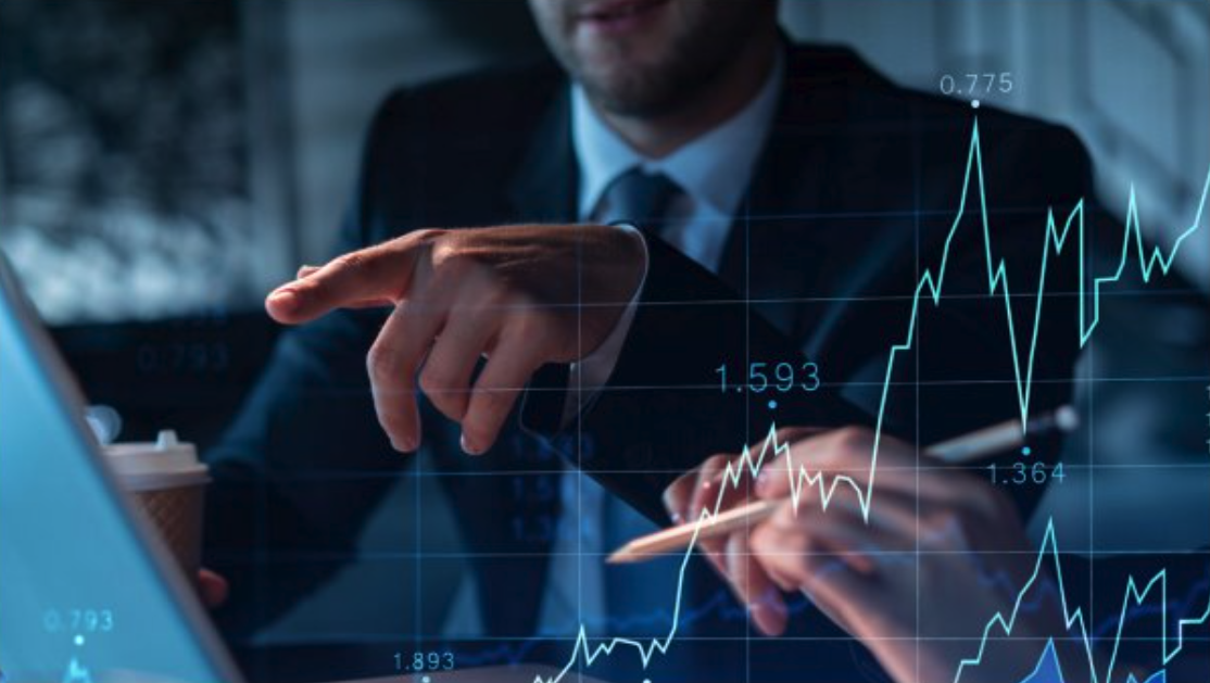 Zwei Personen in Businesskleidung betrachten Finanzdiagramme, die über einen Laptop-Bildschirm gelegt sind
