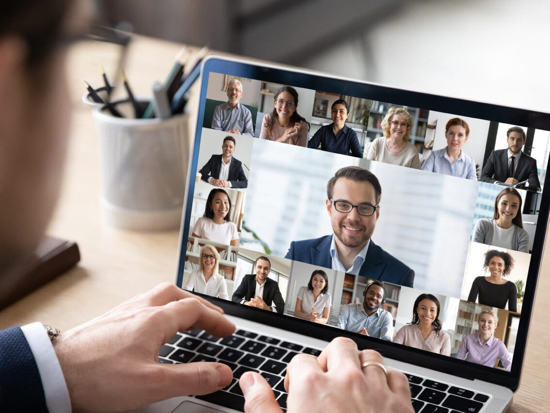 A person is using a laptop for a video conference call, with the screen showing a video call grid of engaged participants. The person typing—who is wondering what is SASE—remains partially visible from behind.