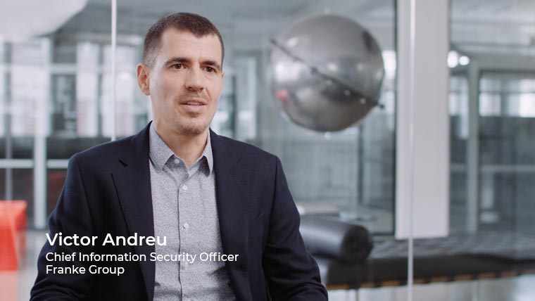 A man in a business suit sits in an office with modern decor, including a large metallic sphere in the background. The text on the image reads: "Victor Andreu, Chief Information Security Officer, Franke Group," a company known for its robust SD-WAN backbone.